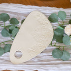 Decorative white stone with embossed patterns on a textured surface with green leaves