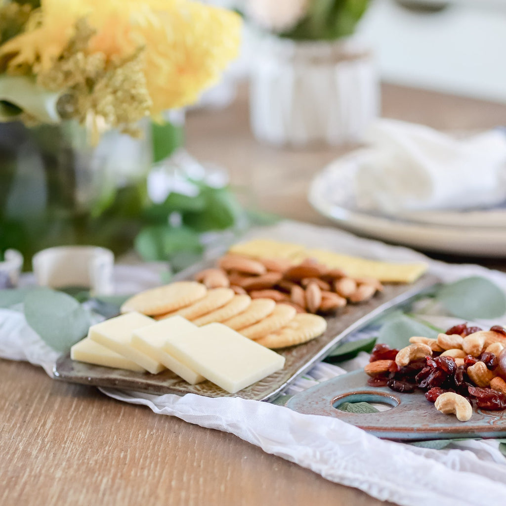 Platter of assorted cheeses and crackers on a wooden table with a decorative background.