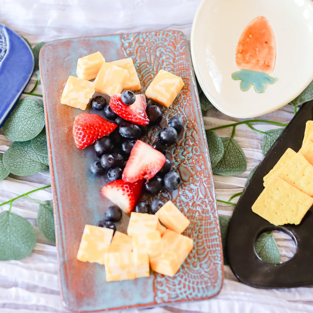 Fruit platter with berries, strawberries, and cantaloupe on a decorative plate with crackers on the side.