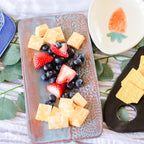 Fruit platter with berries, strawberries, and cantaloupe on a decorative plate with crackers on the side.