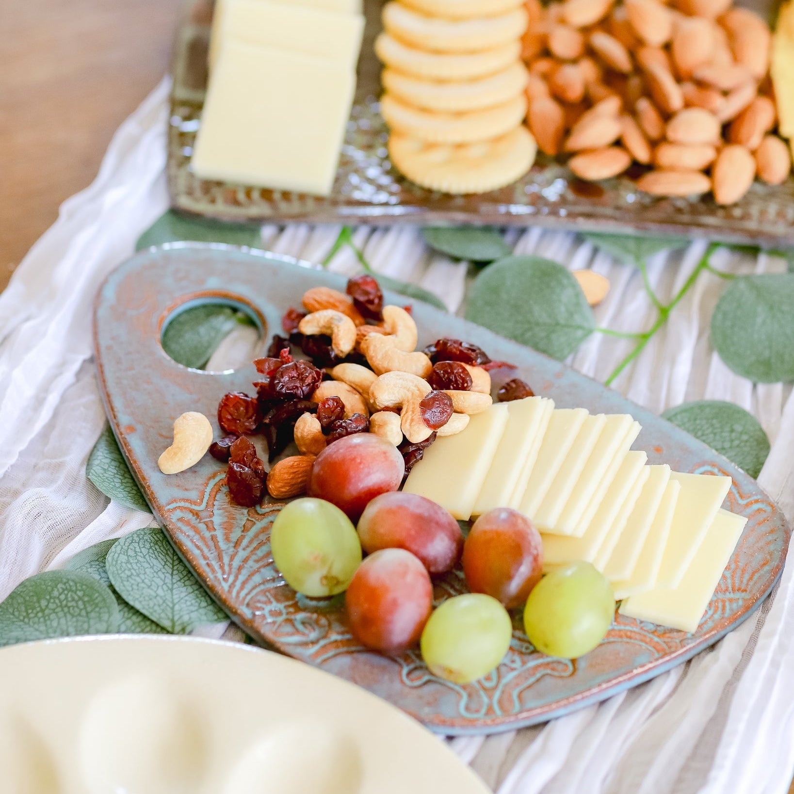 Platter with cheese, fruits, and nuts on a decorative tablecloth