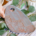 Decorative ceramic tag with floral patterns on a white surface with green leaves.