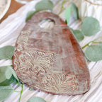 Decorative wooden board with embossed design on a white surface with green leaves