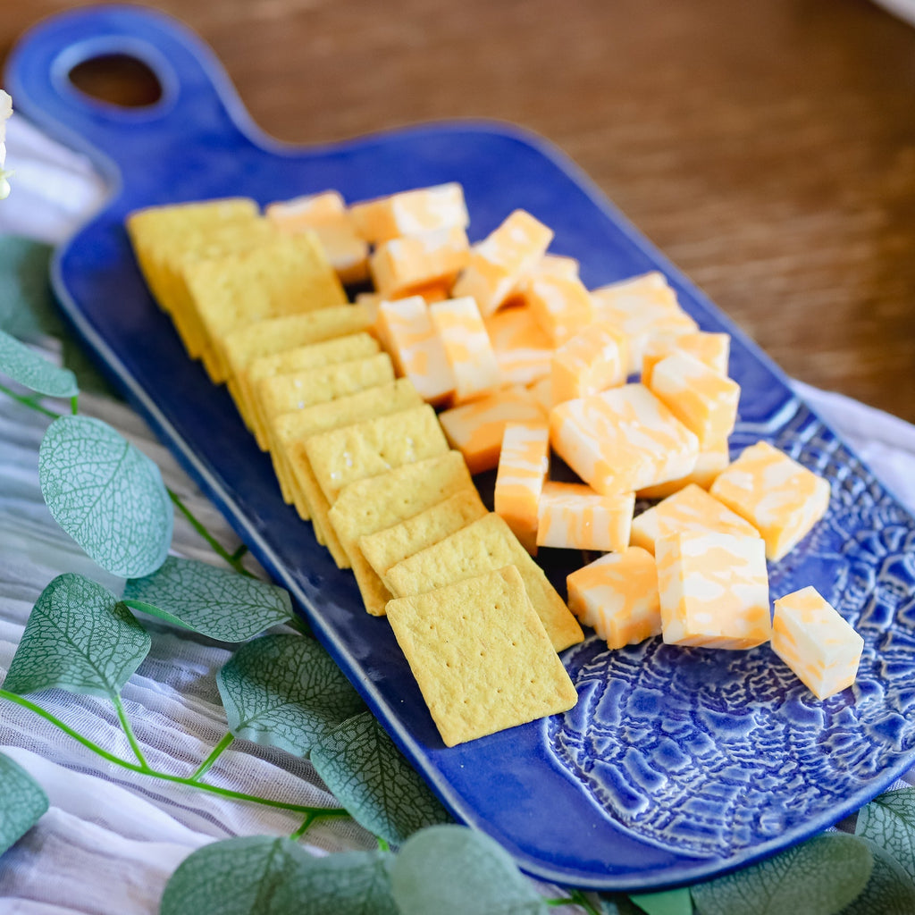 Blue plate with yellow crackers and orange cheese cubes on a wooden surface.