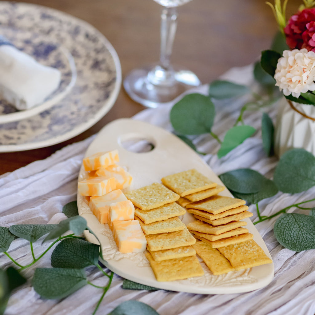 Platter of cheese and crackers on a table with a glass and flowers in the background