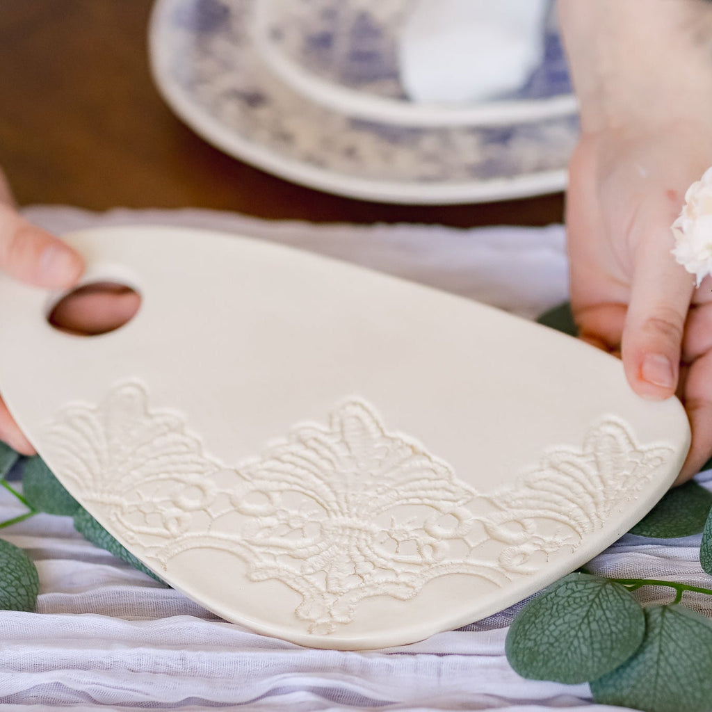 Person holding a white ceramic paddle with floral patterns on a tablecloth.