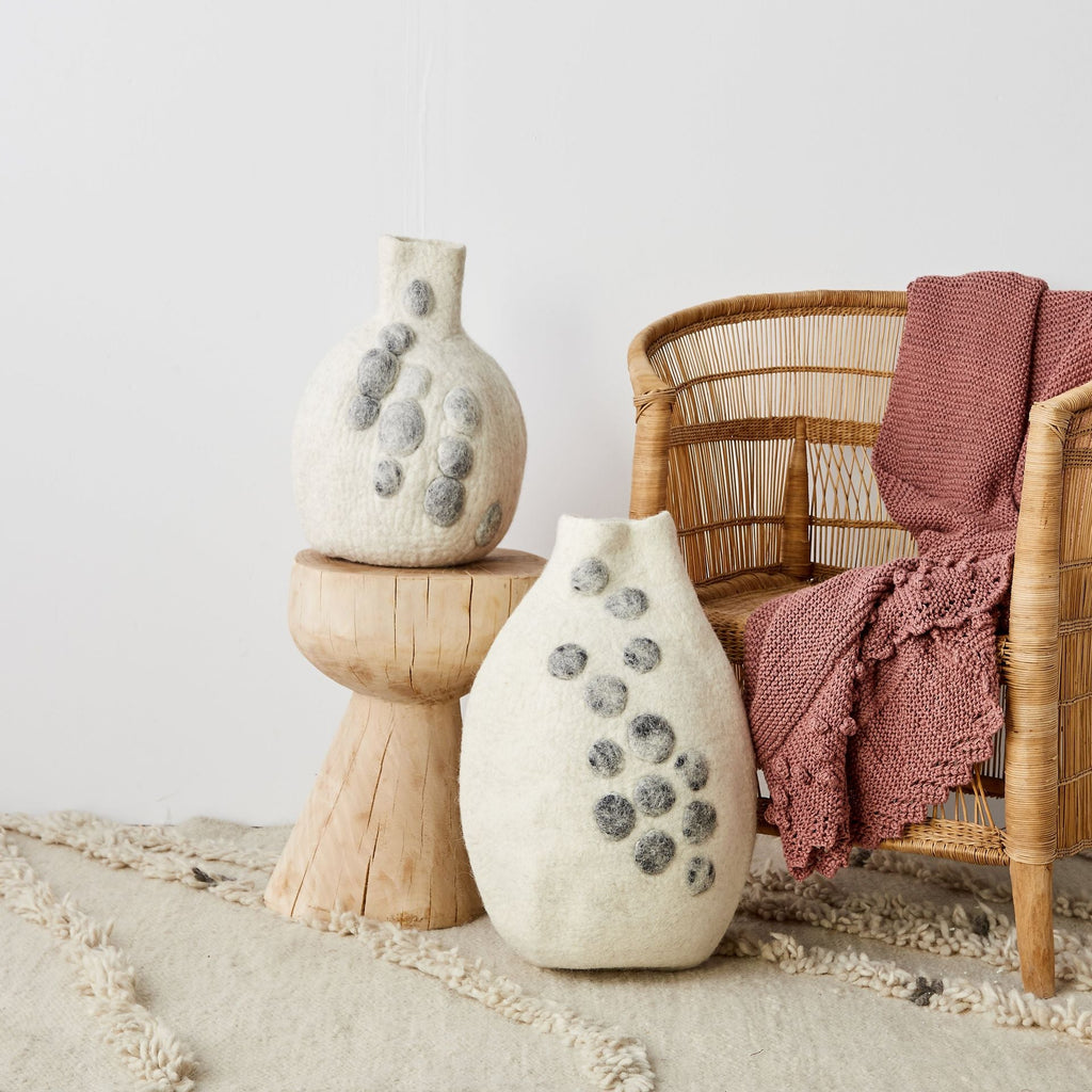 Decorative vases with textured surface on a wooden stand next to a wicker chair with a pink blanket.