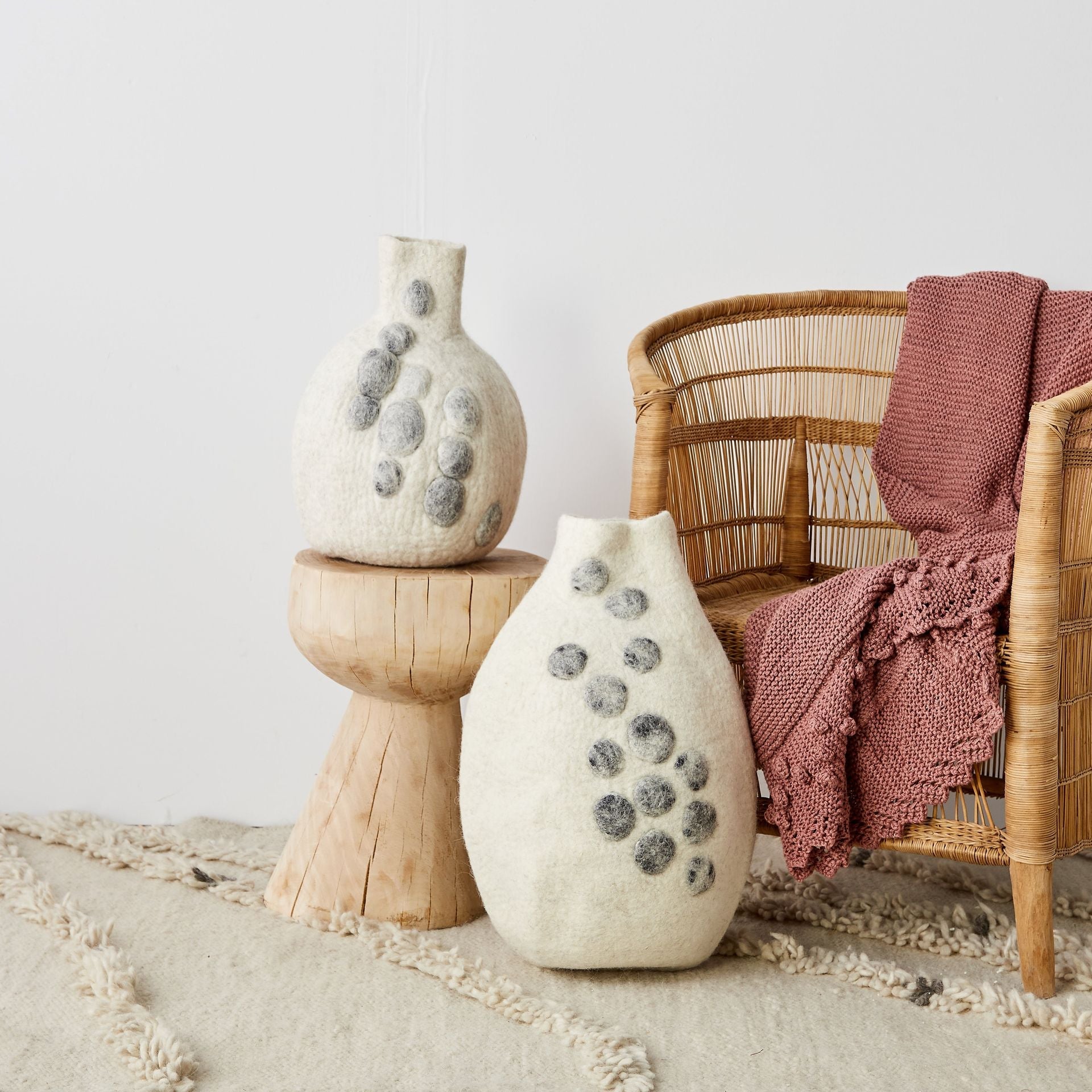 Decorative vases with textured surface on a wooden stand next to a wicker chair with a pink blanket.