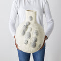Person holding a textured vase with pebble print designs against a plain background