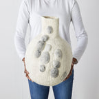 Person holding a textured vase with pebble print designs against a plain background