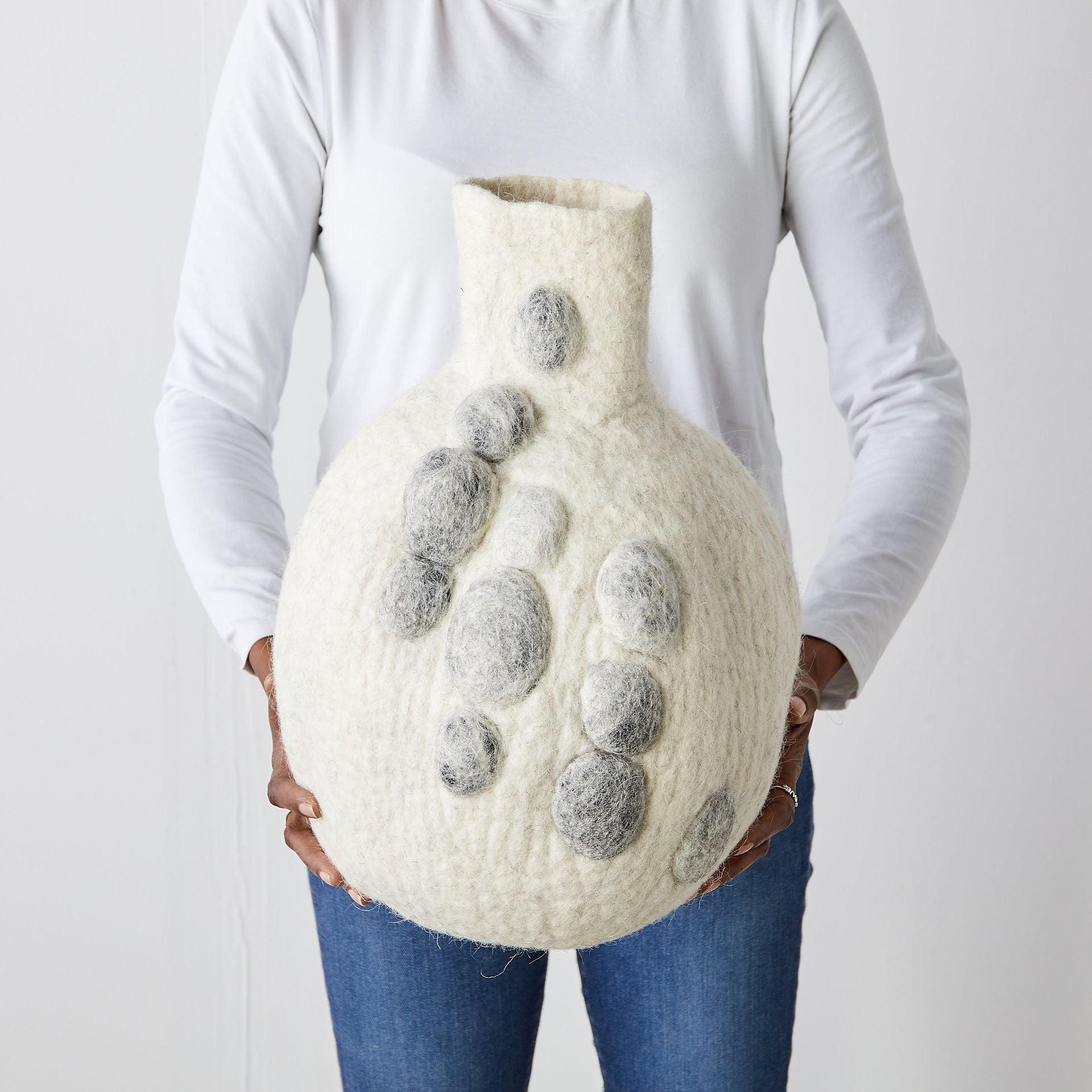 Person holding a textured vase with pebble print designs against a plain background