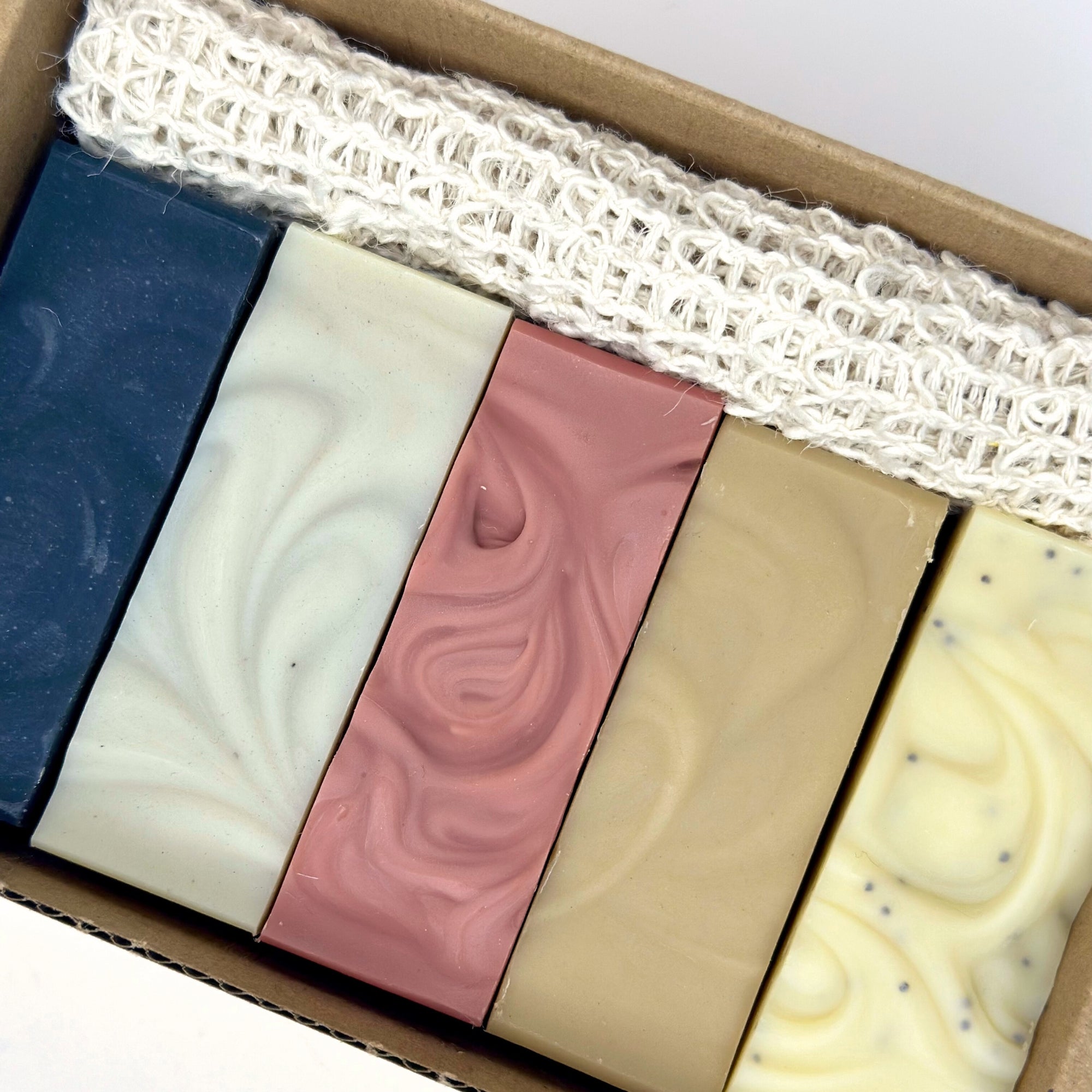 Five different colored soap bars in a box with a white lace background