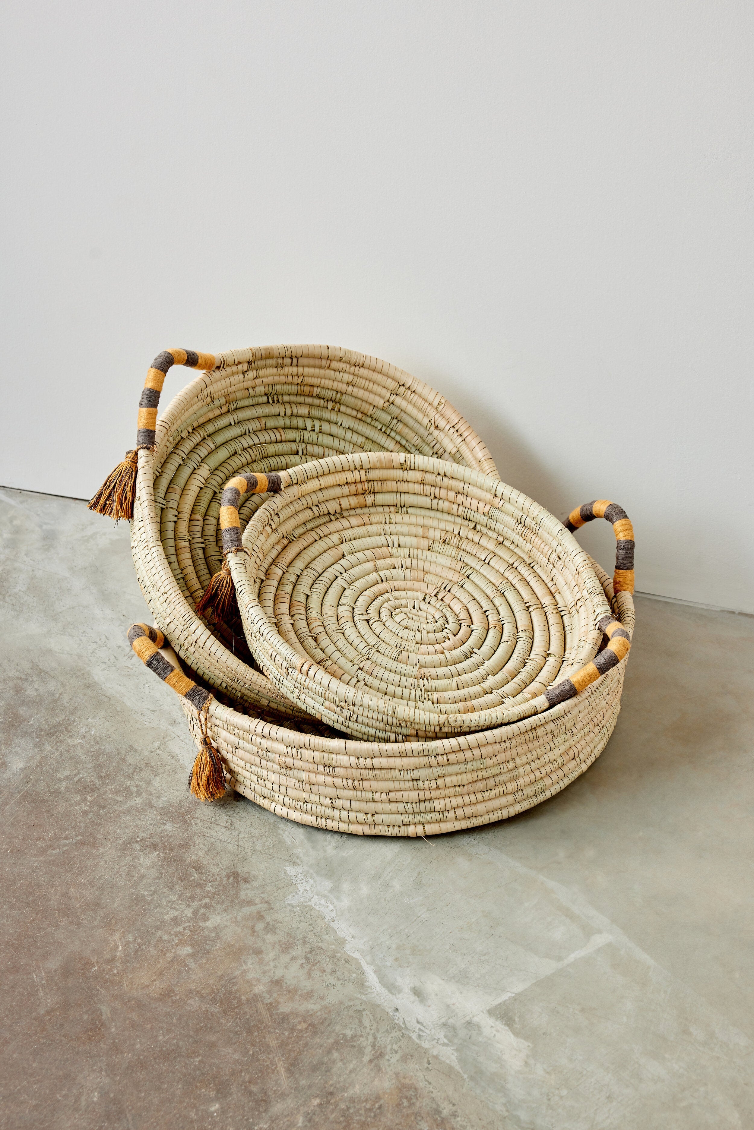 Set of three woven baskets with handles on a concrete surface.