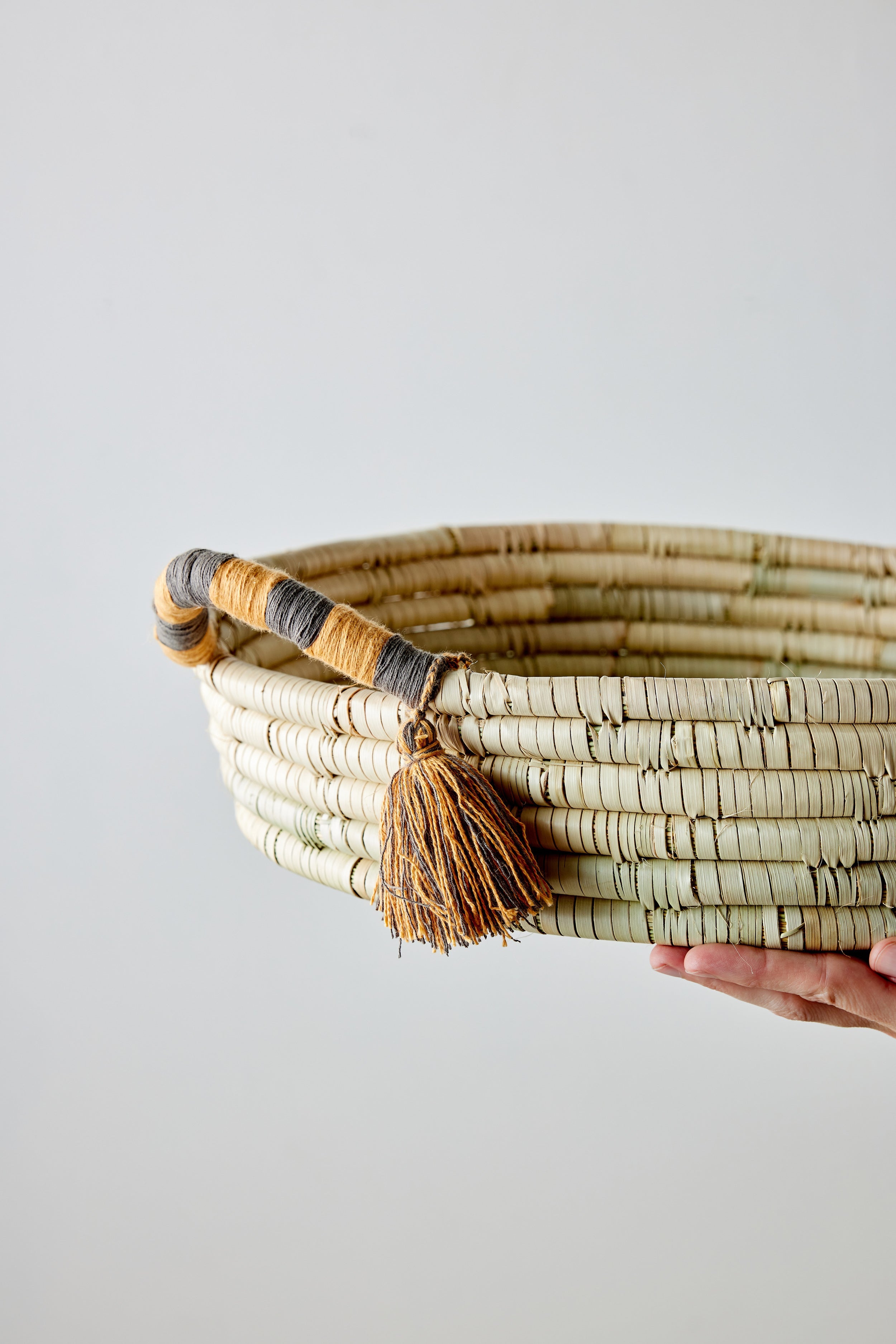 Hand-woven basket with tassel held against a plain background