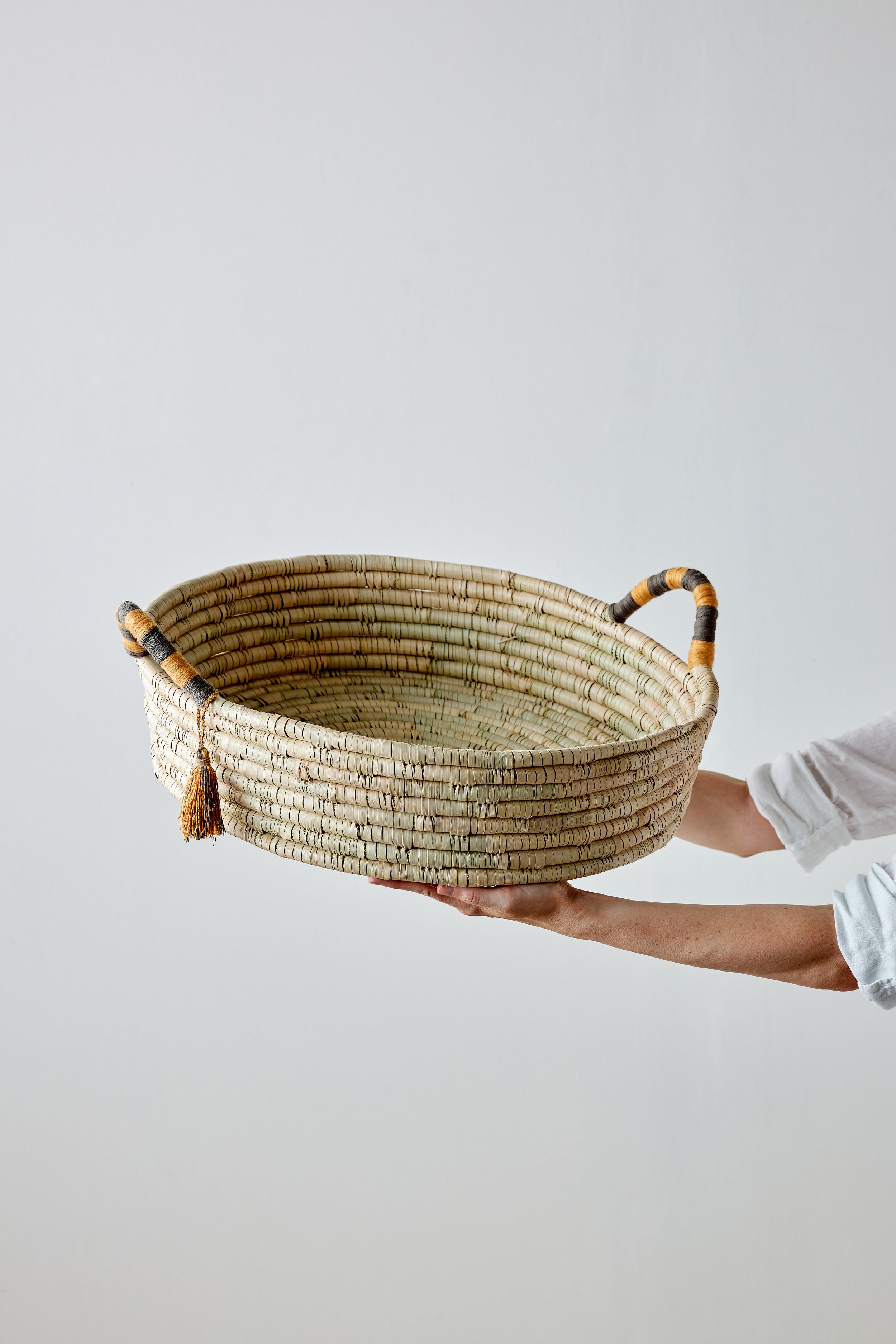 Person holding a woven basket with handles on a light gray background