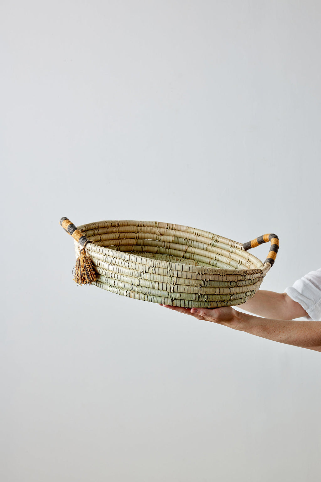 Handheld woven basket with tassels on a plain background