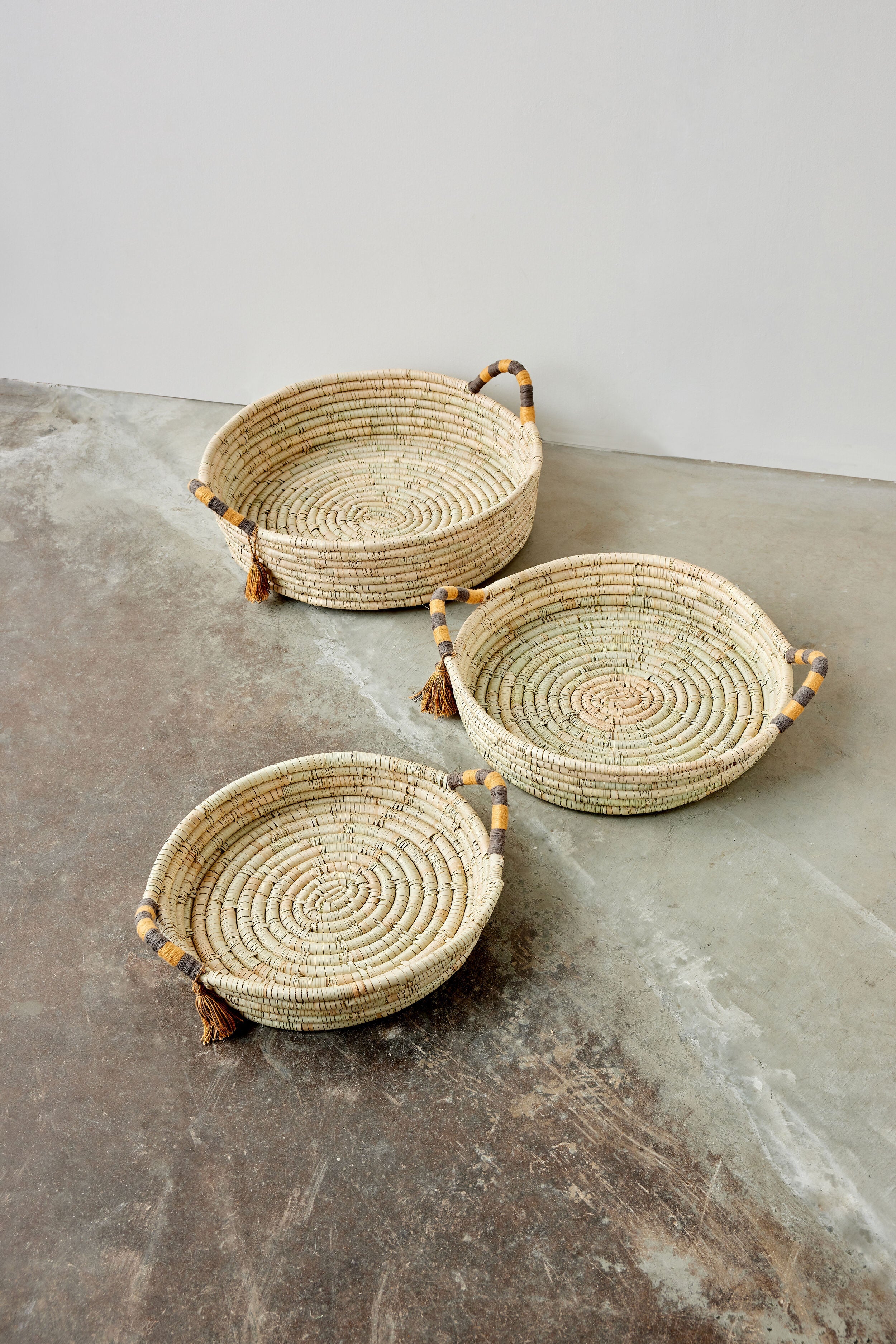 Three woven baskets with handles on a concrete surface