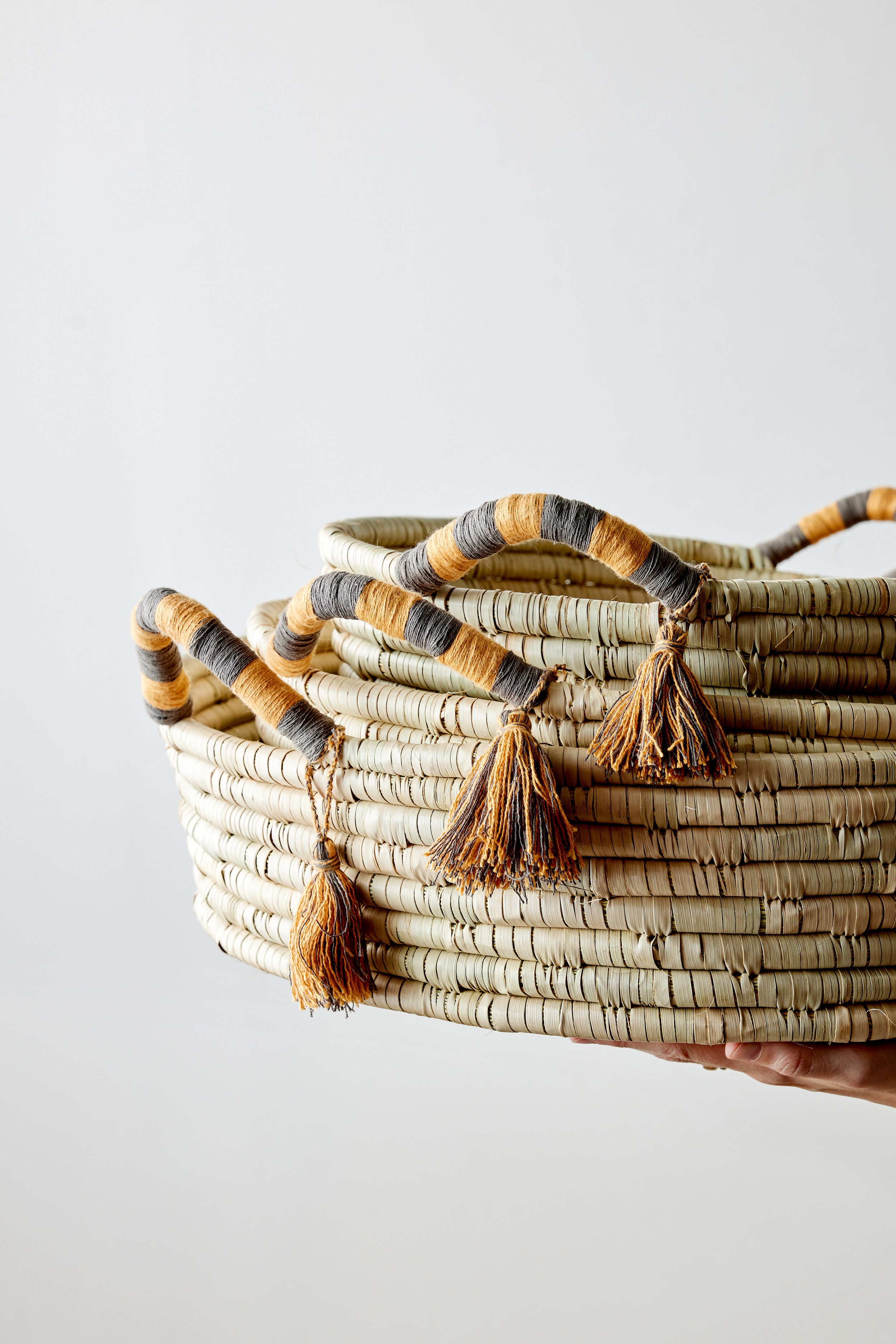 Woven basket with tassels held by a hand on a light background