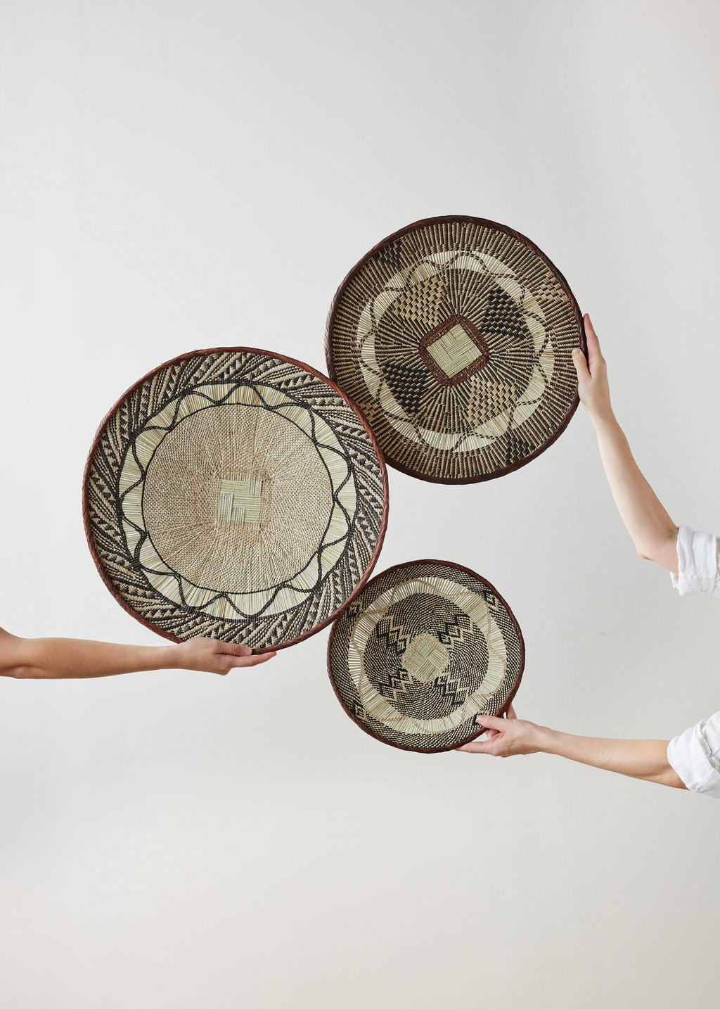 Three woven baskets held by people against a white background
