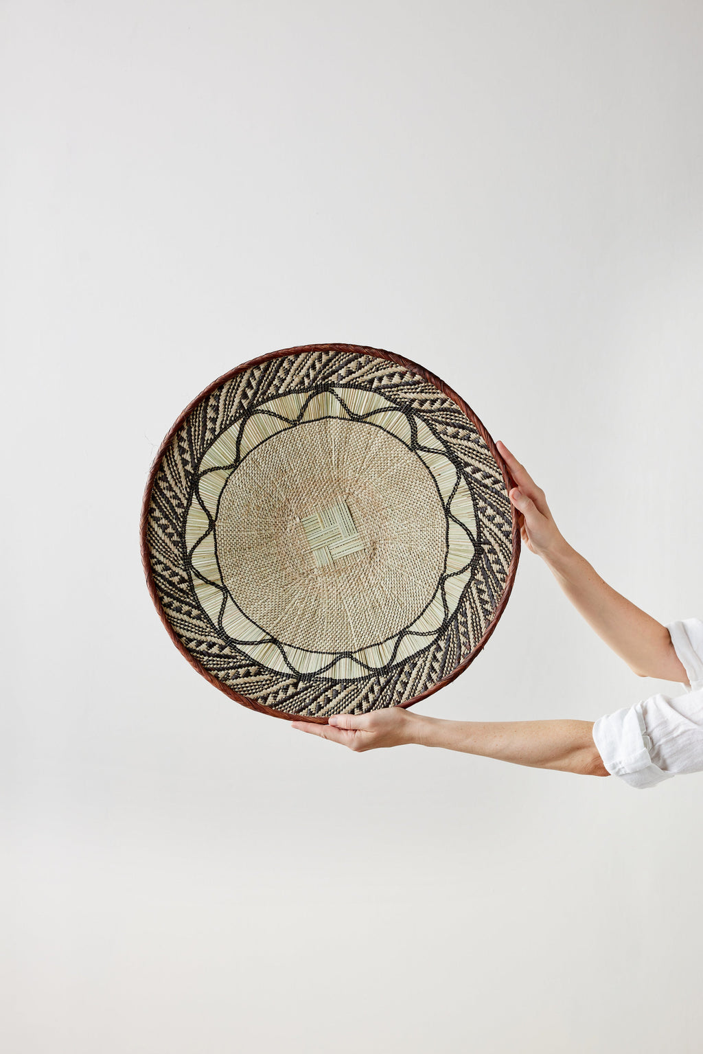 Person holding a round woven basket with decorative patterns on a white background