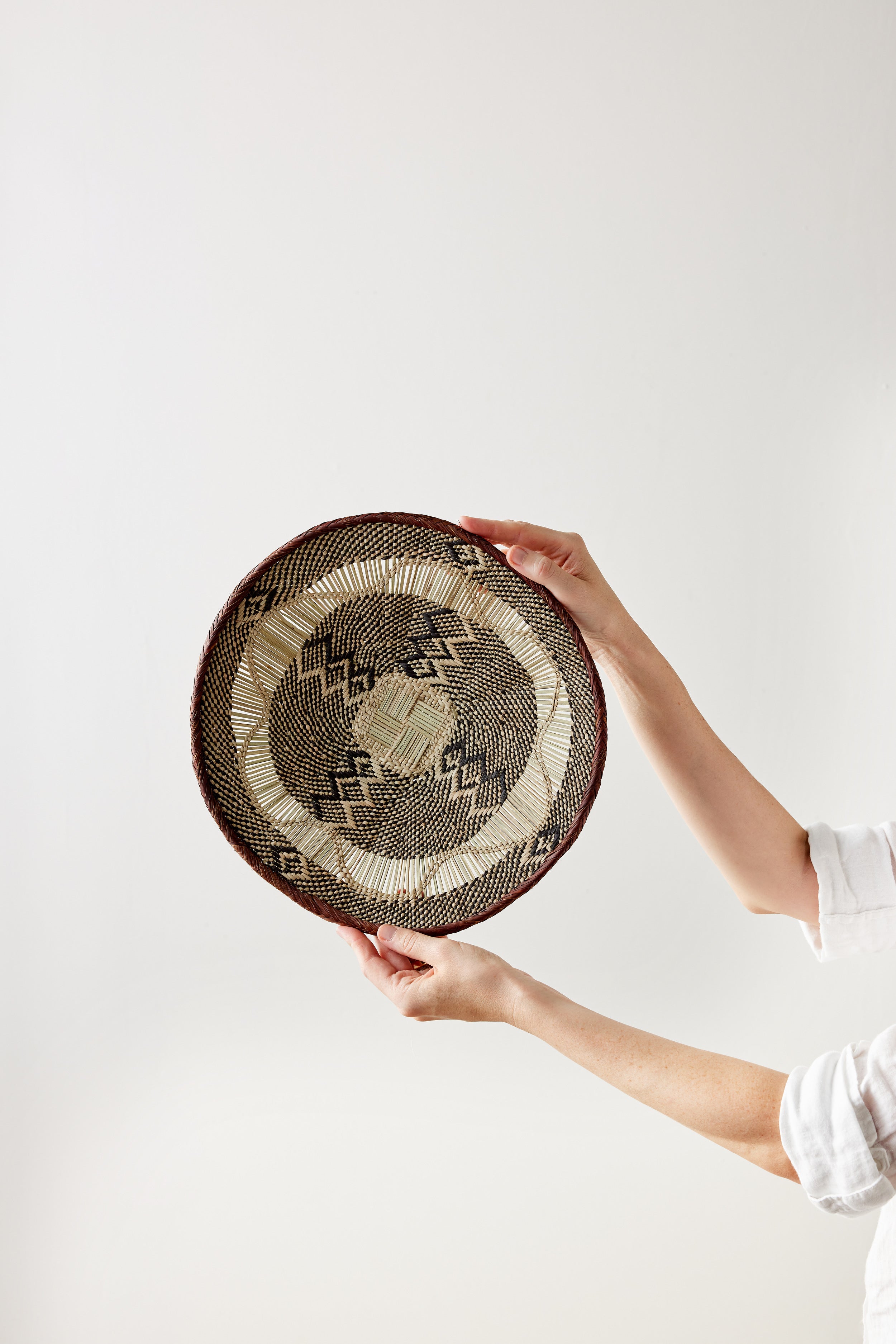 Person holding a woven basket with geometric pattern against a white background