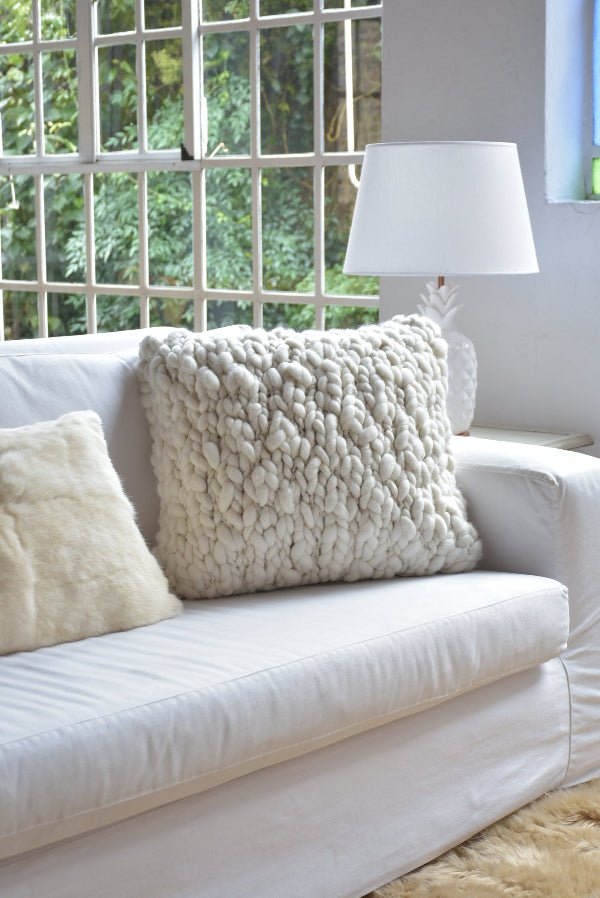 White sofa with textured pillows and a lamp in a room with large windows.