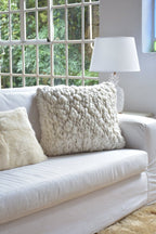 White sofa with textured pillows and a lamp in a room with large windows.