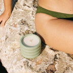 Green candle on a rocky surface with a person in a green bikini bottom.