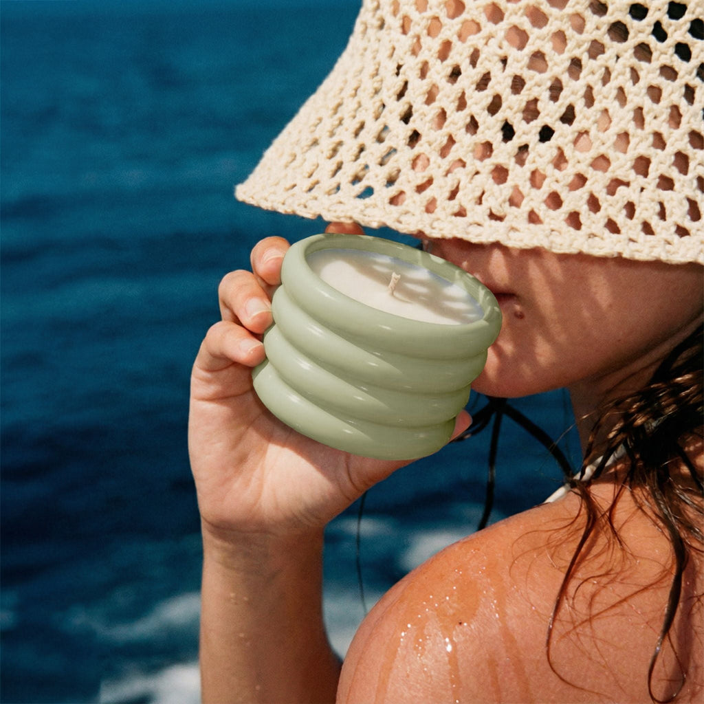 Person holding a light green spiral candle with ocean in the background