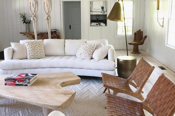 Modern living room with white sofa, wooden coffee table, decorative white pillows, and wicker chairs.