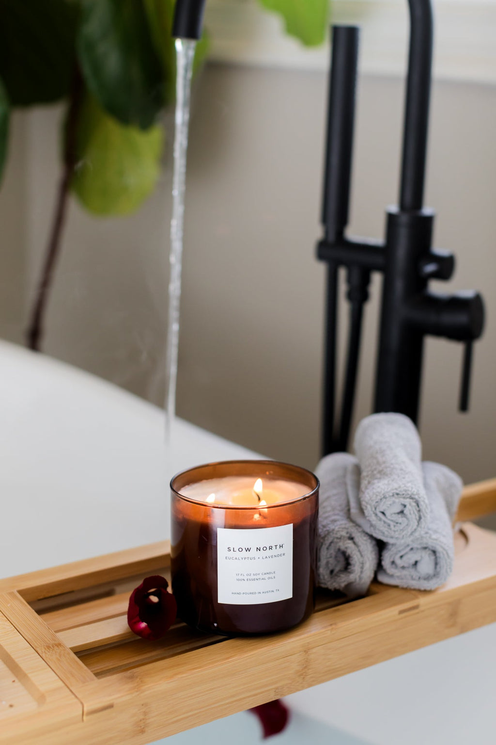 Candle on a bath tray with towels and a plant in the background