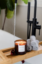 Candle on a bath tray with towels and a plant in the background