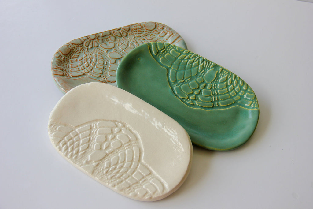 Three ceramic dishes in beige, green, and white with textured patterns on a light gray background.