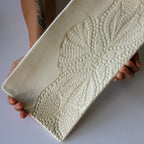 Person holding a textured ceramic dish against a plain background
