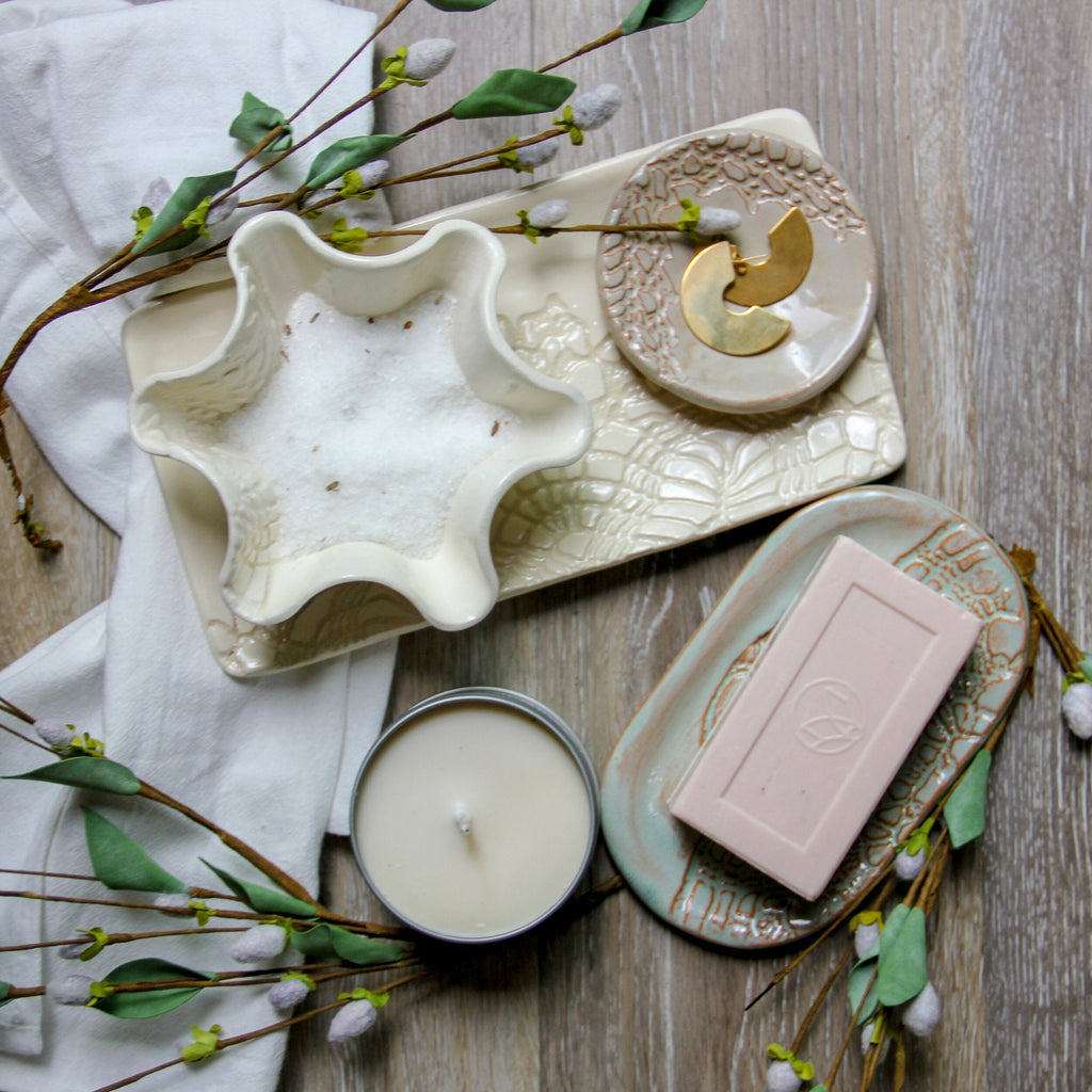 Ceramic dish with star-shaped bowl, candle, and soap on a wooden surface with greenery.