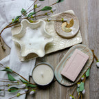 Ceramic dish with star-shaped bowl, candle, and soap on a wooden surface with greenery.