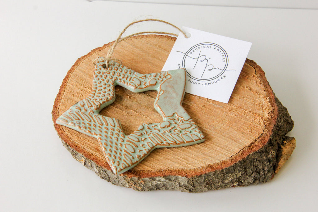 Decorative light green ceramic star ornament on a wooden slice with a tag