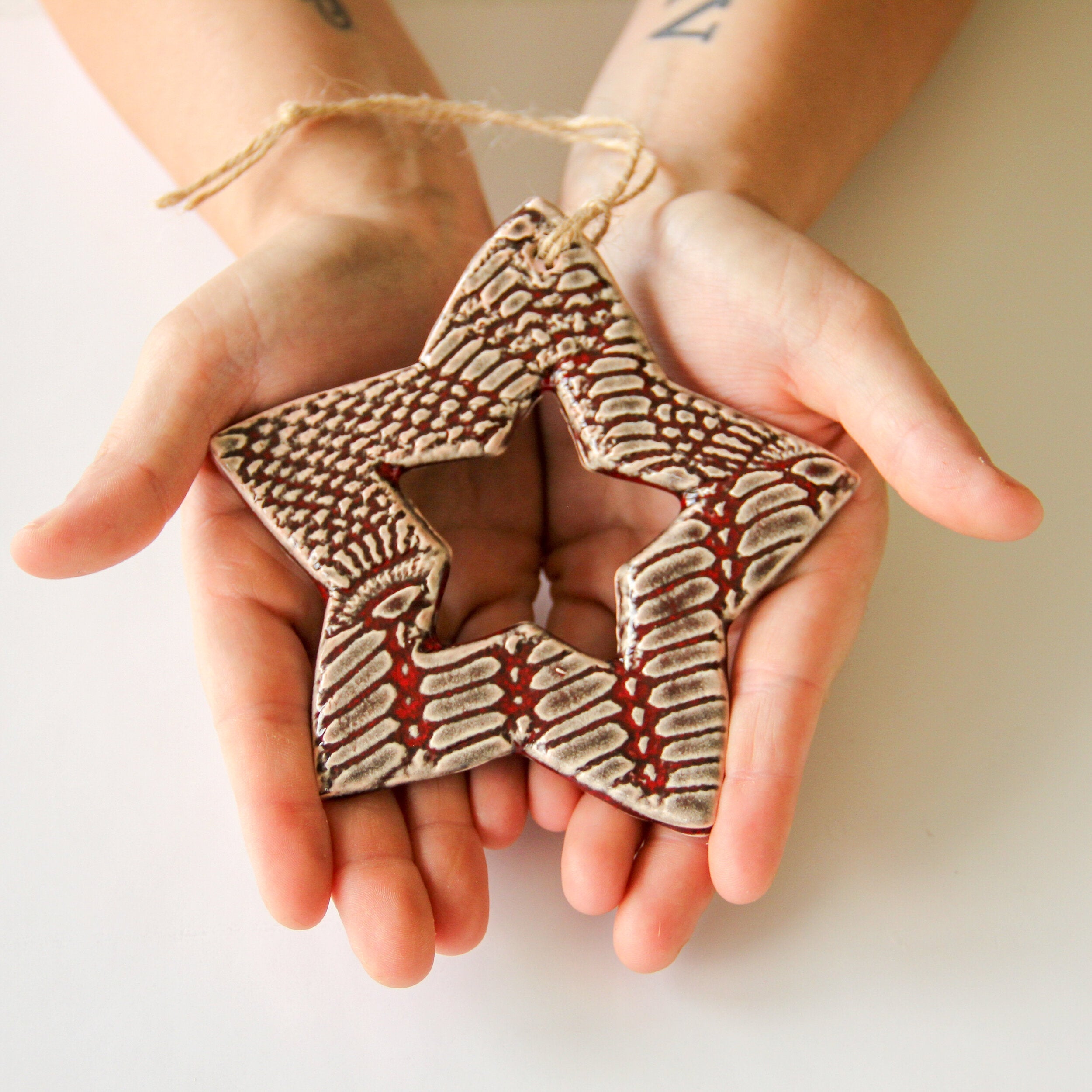 Two hands holding a ceramic star-shaped ornament with a textured surface.
