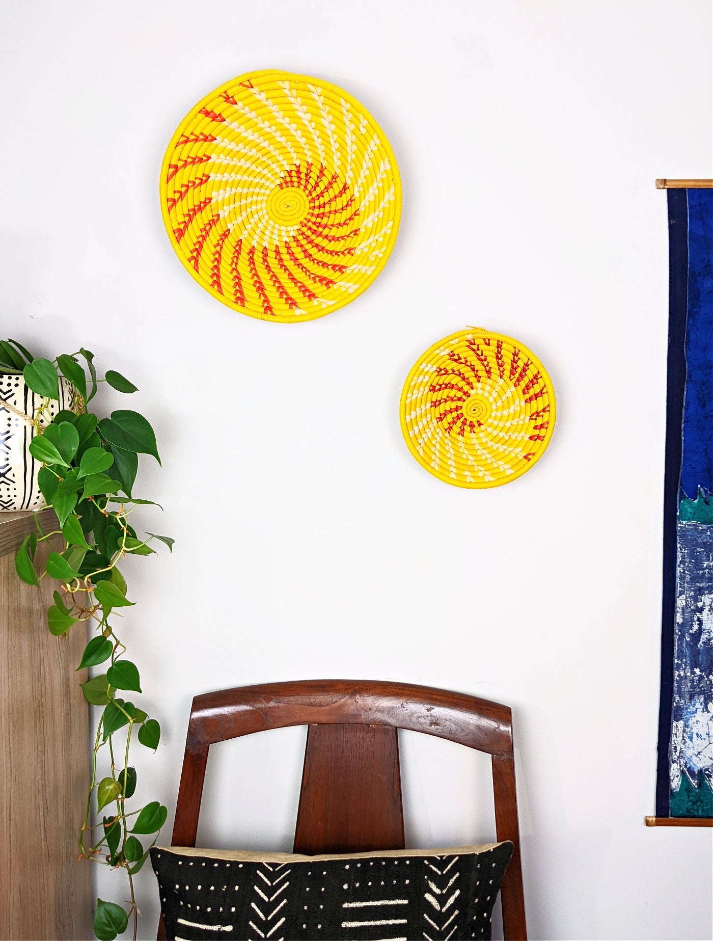Two yellow circular wall decorations with red patterns on a white wall, with a wooden chair and plant in the foreground.