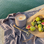 Candle, figs, and a hat on a cloth by a body of water