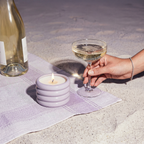 Hand holding a glass of champagne next to a lit candle and a wine bottle on a textured surface