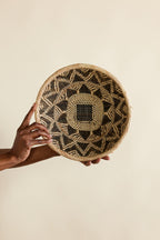 Hand holding a woven basket with geometric pattern on a beige background