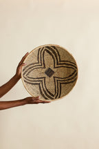 Person holding a woven basket with geometric pattern against a beige background
