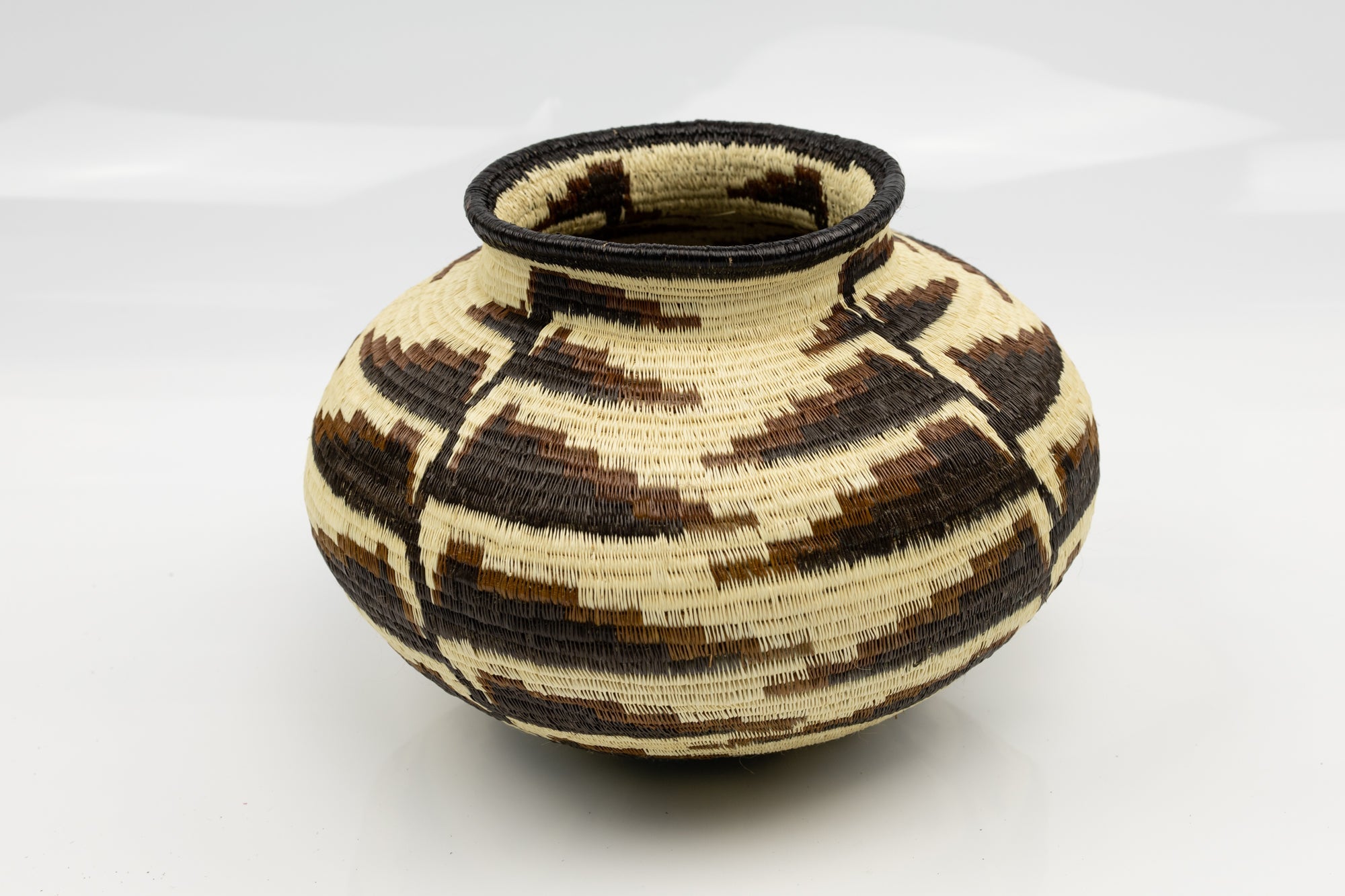 Woven basket with black and beige pattern on a white background