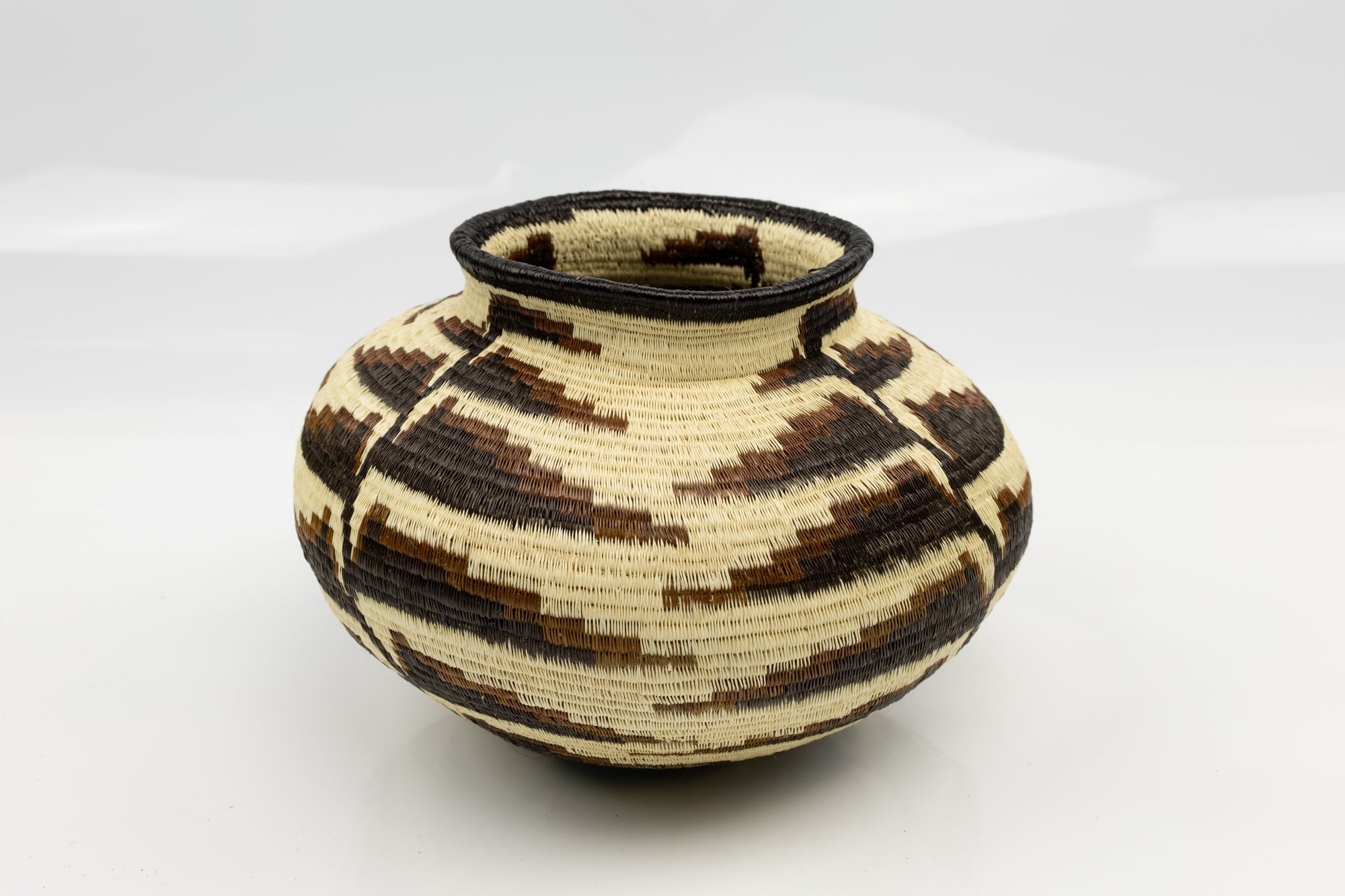 Handwoven basket with black and beige pattern on a white background