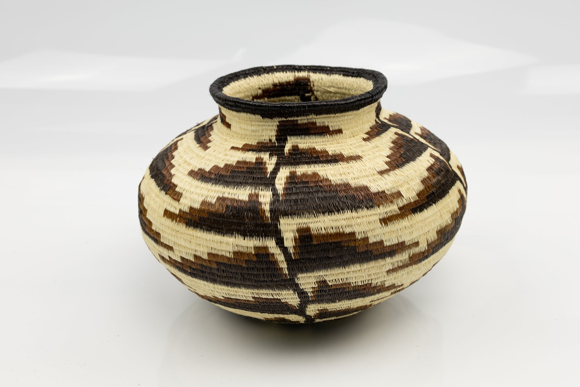 Woven basket with black and beige pattern on a white background