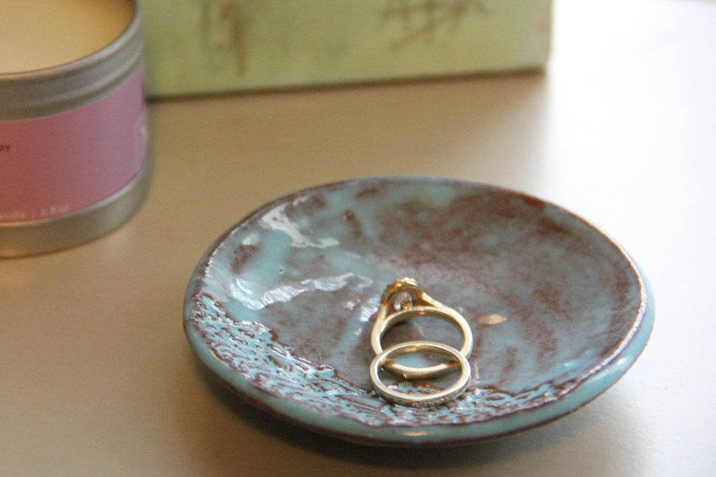 Teal ceramic dish with gold rings on a light surface next to a pink candle.