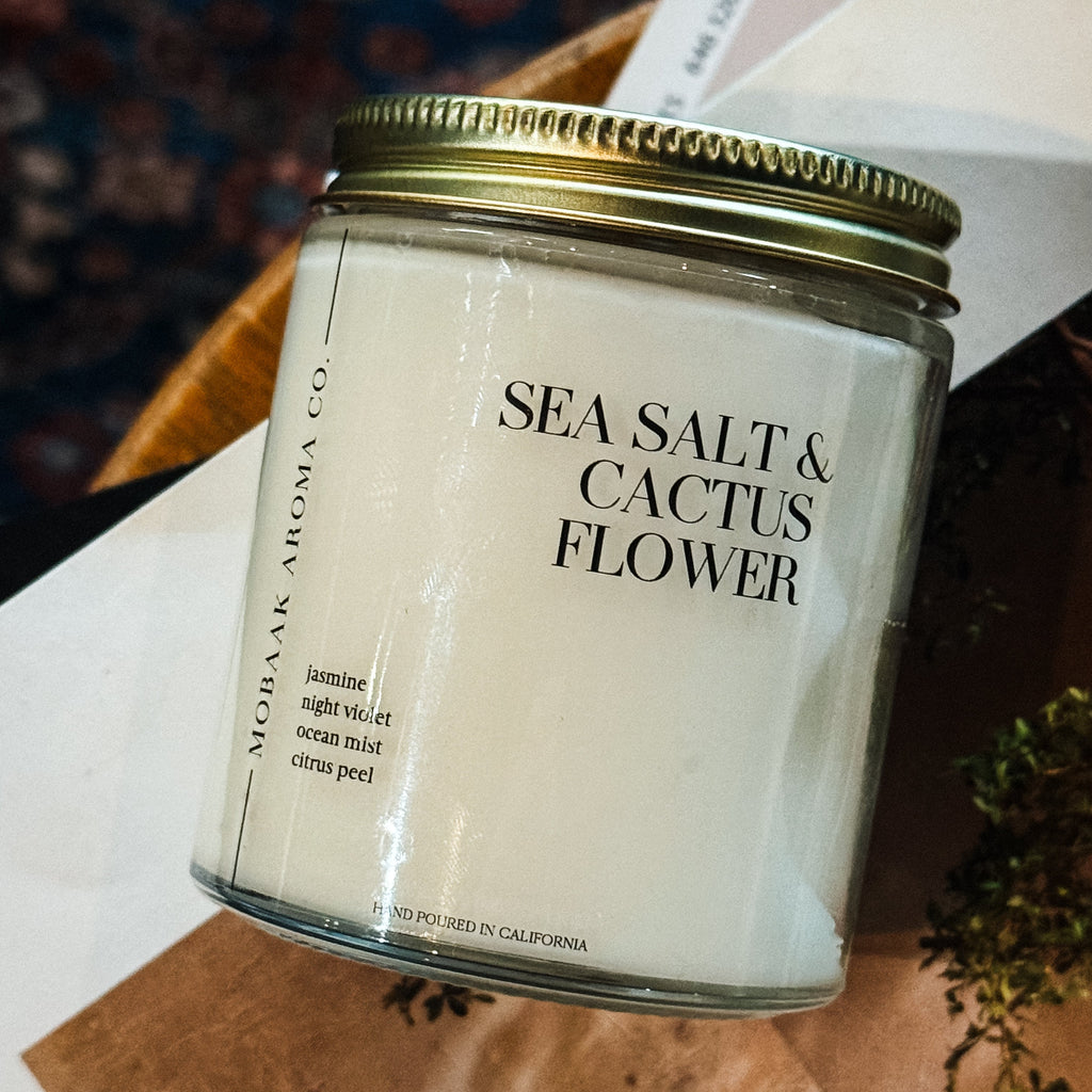 Candle jar labeled 'Sea Salt & Cactus Flower' on a wooden surface.