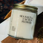 Candle jar labeled 'Sea Salt & Cactus Flower' on a wooden surface.