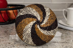 Round woven basket bottom with black, brown, and beige pattern on a kitchen counter.